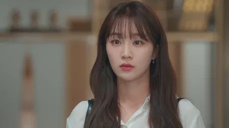 Mujer joven con flequillo, con aspecto pensativo en el episodio 1.