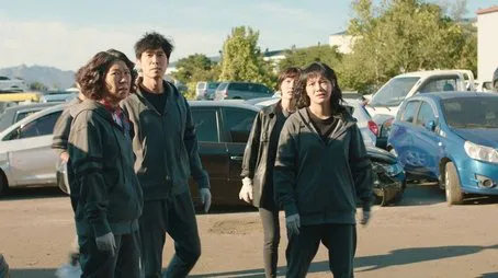 Cuatro personas con ropa de trabajo se encuentran entre coches averiados en un desguace Episodio 01