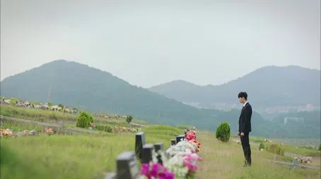Hombre de traje visitando tumbas en un cementerio con vistas a las colinas