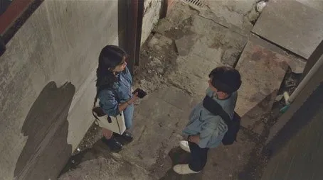 Un hombre y una mujer jóvenes se encuentran en un callejón poco iluminado, posiblemente discutiendo sobre el destino.
