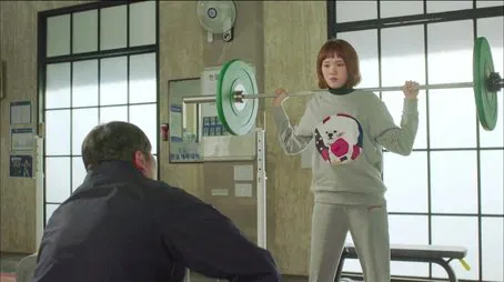 Mujer levantando pesas en el gimnasio durante el episodio 02.