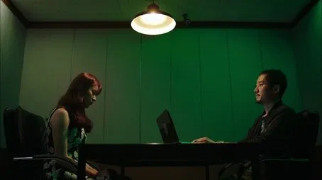 Un hombre y una mujer se sientan a una mesa trabajando con sus portátiles Un misterioso ambiente en una habitación verde