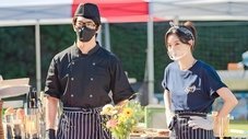 Dos chefs con mascarillas se encuentran en un puesto de comida al aire libre.