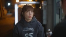 Mujer joven con sudadera gris oscura y aspecto pensativo. Episodio 7.